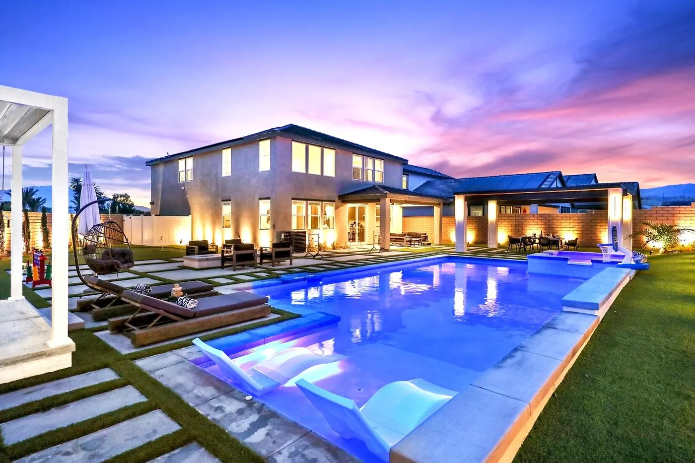 Long pool glowing at twilight beside a modern two-story home